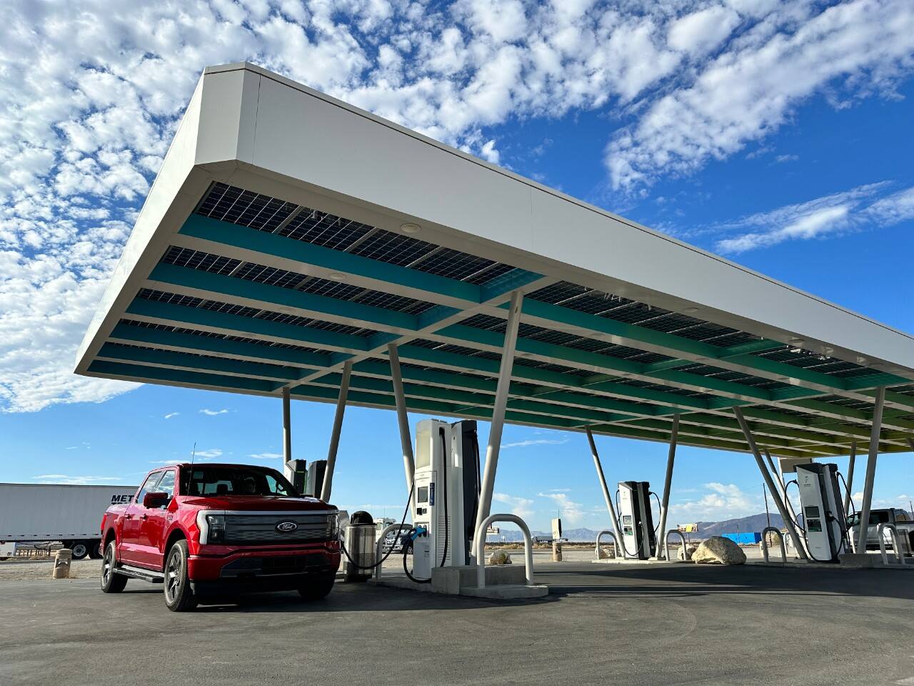 A red F-150 Lightning is charging under an awning.